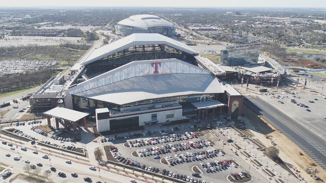 An aerial view of a stadium with a large T-shaped structure, parking lots, and surrounding infrastructure.