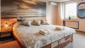 Ein Schlafzimmer mit einem großen Bett, einem Nachttisch, einer Wand-Klimaanlage, einem Fenster mit Aussicht und einem Bild von einem Steg.
