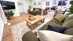 A modern living room with a sofa, coffee table, and a TV. There is a kitchen in the background with a dining area. - Stylish Newly-Renovated Home in a Central Location (Thunder Bay)