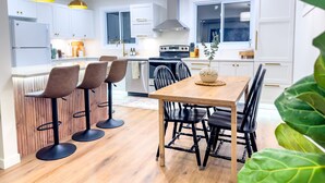A modern kitchen with white cabinets, a wooden dining table, and black bar stools. - Stylish Newly-Renovated Home in a Central Location (Thunder Bay)