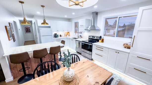 A modern kitchen with white cabinets, a central island with seating, stainless steel appliances, and pendant lighting. - Stylish Newly-Renovated Home in a Central Location (Thunder Bay)
