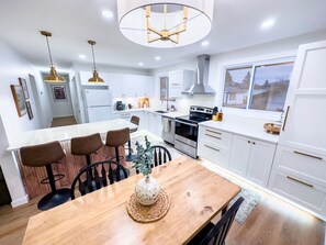 A modern kitchen with white cabinets, a central island with seating, stainless steel appliances, and pendant lighting. - Stylish Newly-Renovated Home in a Central Location (Thunder Bay)
