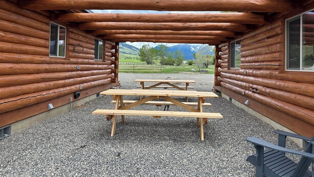 Una cabaña de troncos con un patio de grava, una mesa de picnic de madera y vistas a la montaña.