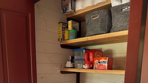 Un lavadero con dos lavadoras de carga frontal, estantes con cajas de almacenamiento y una puerta de madera.