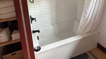 A modern bathroom with a glass-enclosed shower, white tiled walls, and a built-in shelf with toiletries.