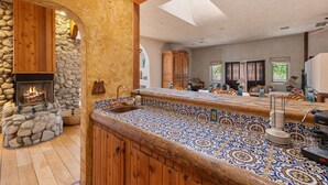 A kitchen with a stone fireplace, wooden cabinets, and a tiled backsplash. - Lockout The Oasis | Natural Mineral Hot Springs on 107 Acres (Desert Hot Springs)