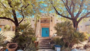 A wooden staircase leading to a blue door, surrounded by various plants and rocks. - Lockout The Oasis | Natural Mineral Hot Springs on 107 Acres (Desert Hot Springs)