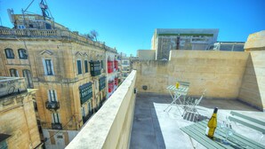 Une terrasse sur le toit, avec une table et des chaises, une bouteille de vin et une vue sur des bâtiments historiques.