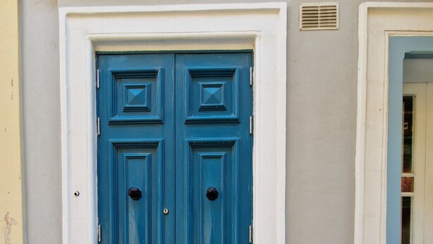 Une porte bleue à deux battants, avec une petite fenêtre sur le côté droit.