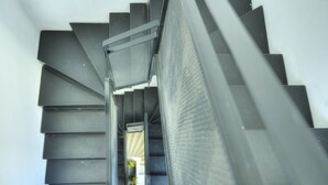 Un escalier moderne avec une rampe en métal, donnant sur une pièce où se trouvent un lit et une plante.