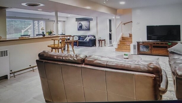 Una sala de estar moderna con un sofá de cuero, un comedor, una escalera y un televisor.