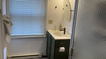 Een badkamer met een raam, een wastafel, een spiegel en een douche.