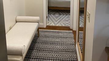 A small, narrow room with a bed, a bench, a mirror, and a patterned rug.