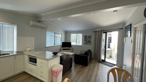 Een ruimtelijk ingerichte leefruimte met kitchenette, een eethoek en een zithoek met een bank en een fauteuil.