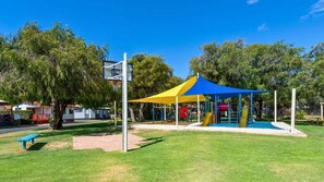 A playground with a basketball hoop, a shaded play area, and a picnic bench. - Budgie Smuggler - Cabin 96 GBHP (West Busselton)