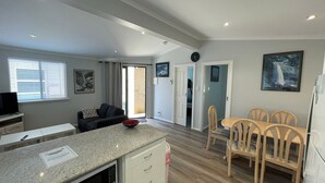 Een moderne keuken met granieten aanrecht, een eetgedeelte met houten stoelen, en een woonkamer met een bank en een televisie.