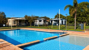 A swimming pool with a tiled deck, surrounded by a fence, and adjacent to a building with a covered patio area. - Budgie Smuggler - Cabin 96 GBHP (West Busselton)
