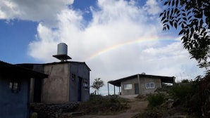 A rural setting with two buildings, one with a water tank on top, and a visible rainbow in the background. - Monoamb. private bathroom to première in full Center (San Francisco del Monte de Oro)