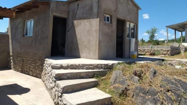 Un edificio pequeño de una sola planta, con base de piedra y fachada de hormigón. Se observa una ventana pequeña en un lateral y una puerta que da al interior.