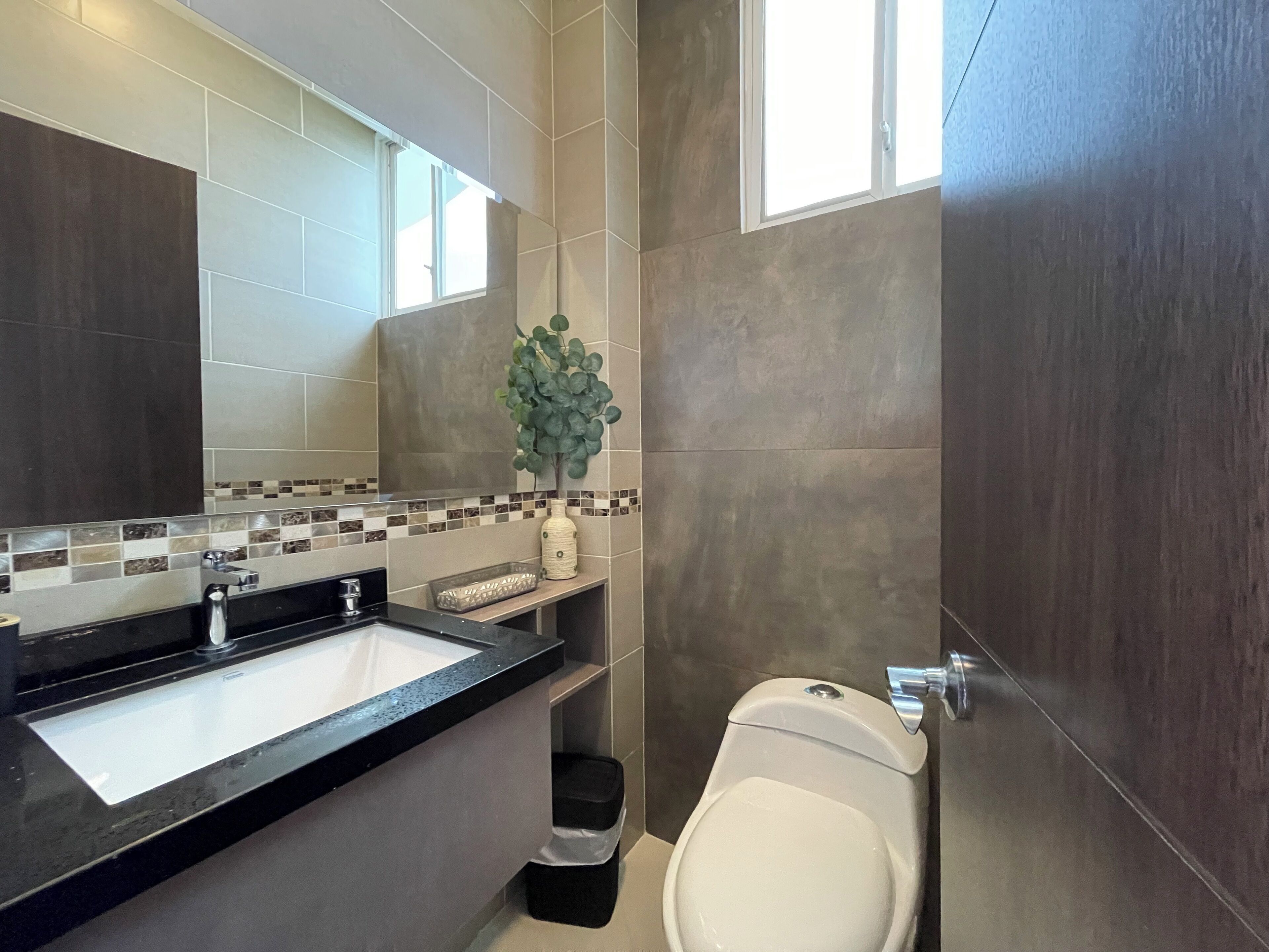 A modern bathroom with a black countertop, a white sink, a toilet, and a small trash bin.