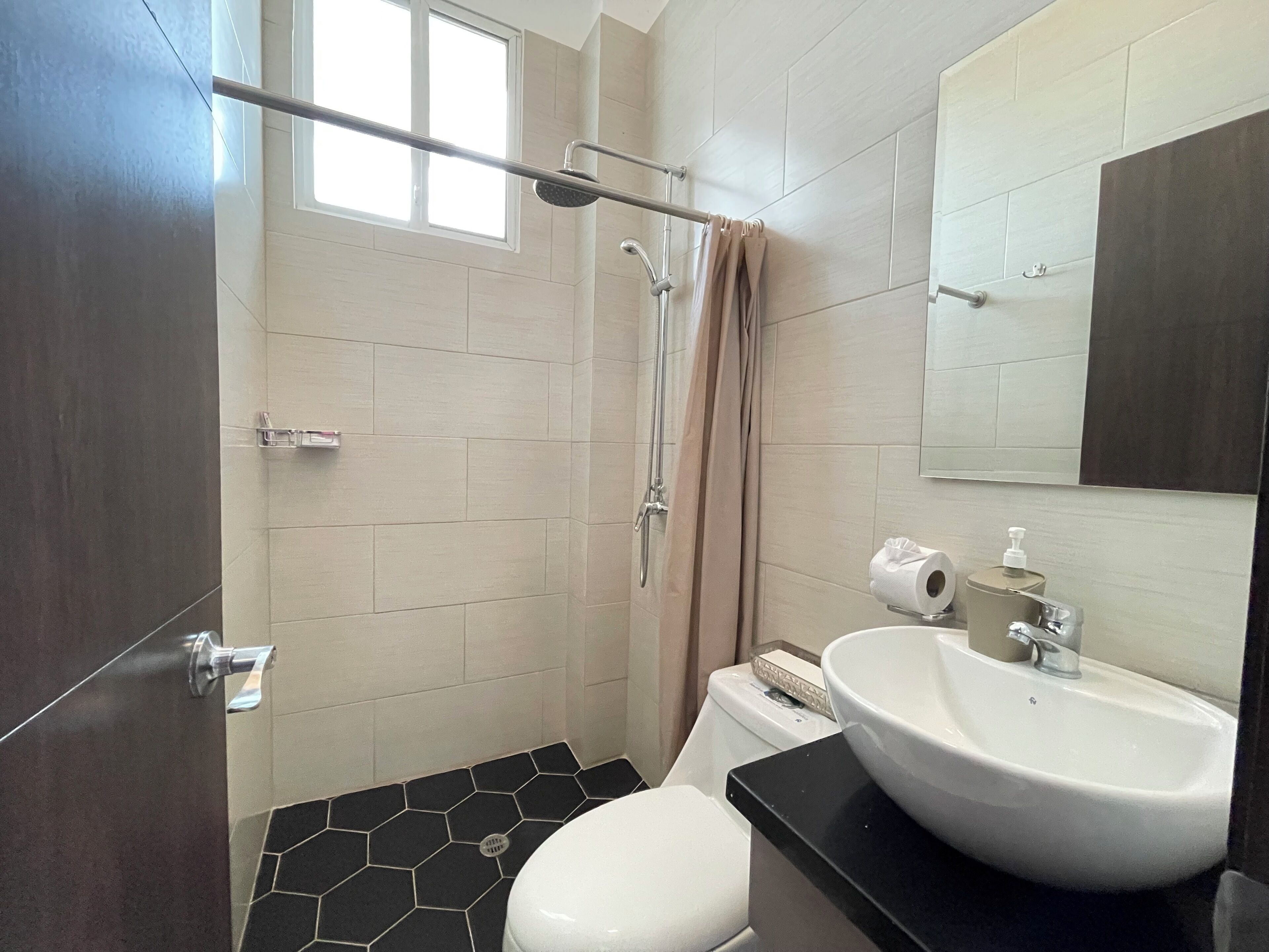 A bathroom with a shower, toilet, sink, and a window.