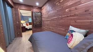 Une chambre avec un mur en bois, un lit avec des oreillers et une porte qui donne sur une autre pièce.