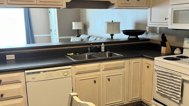 A kitchen with white cabinets, a black countertop, a stove, and a microwave.