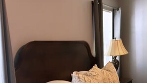 A neatly made bed with white and patterned pillows, a dark headboard, and a bedside lamp.