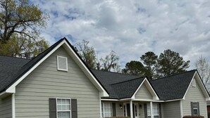 A row of single-story houses with grey siding and black roofs, each with a front porch and a small front yard.