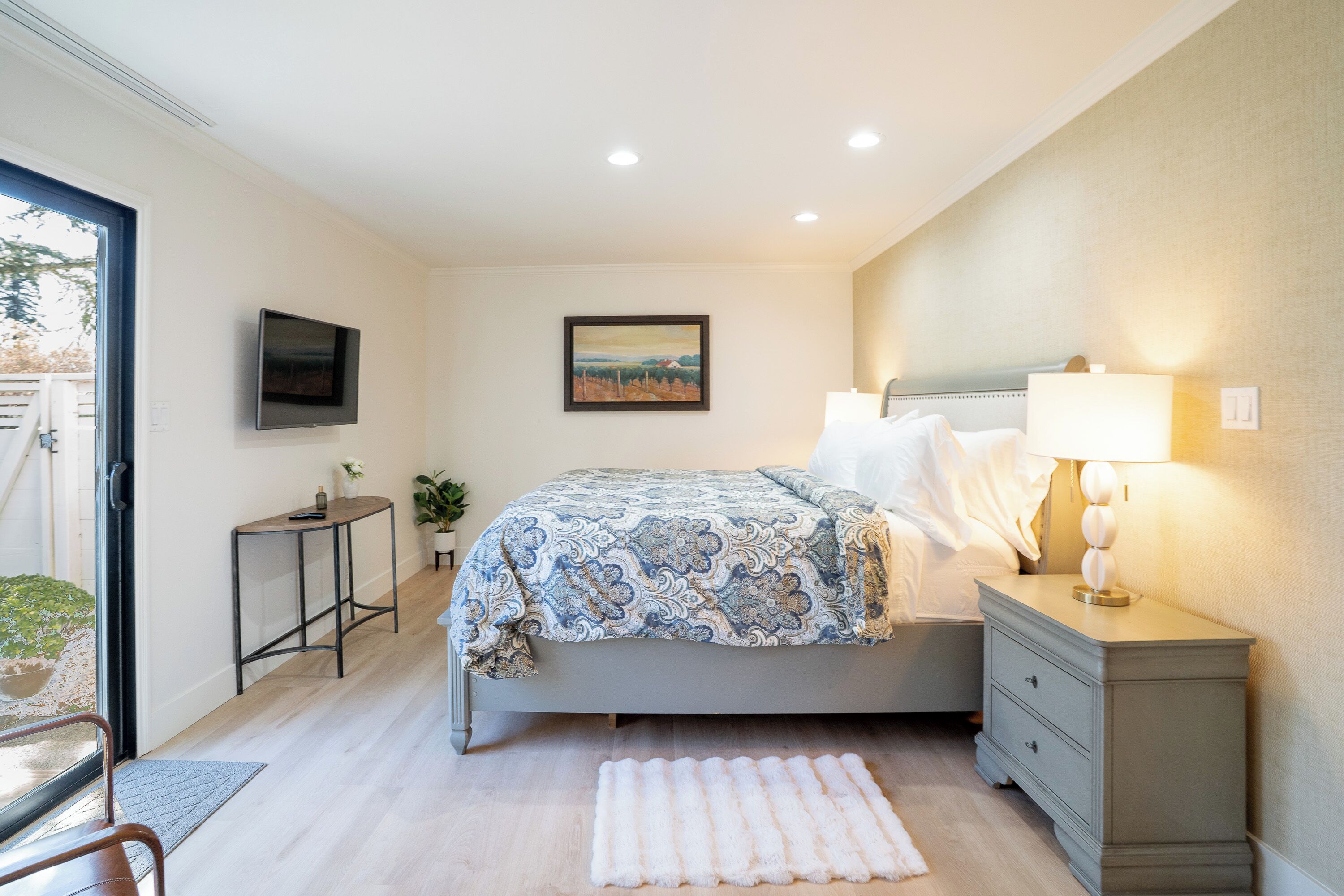 A bedroom with a bed, bedside table, lamp, TV, and a painting on the wall.