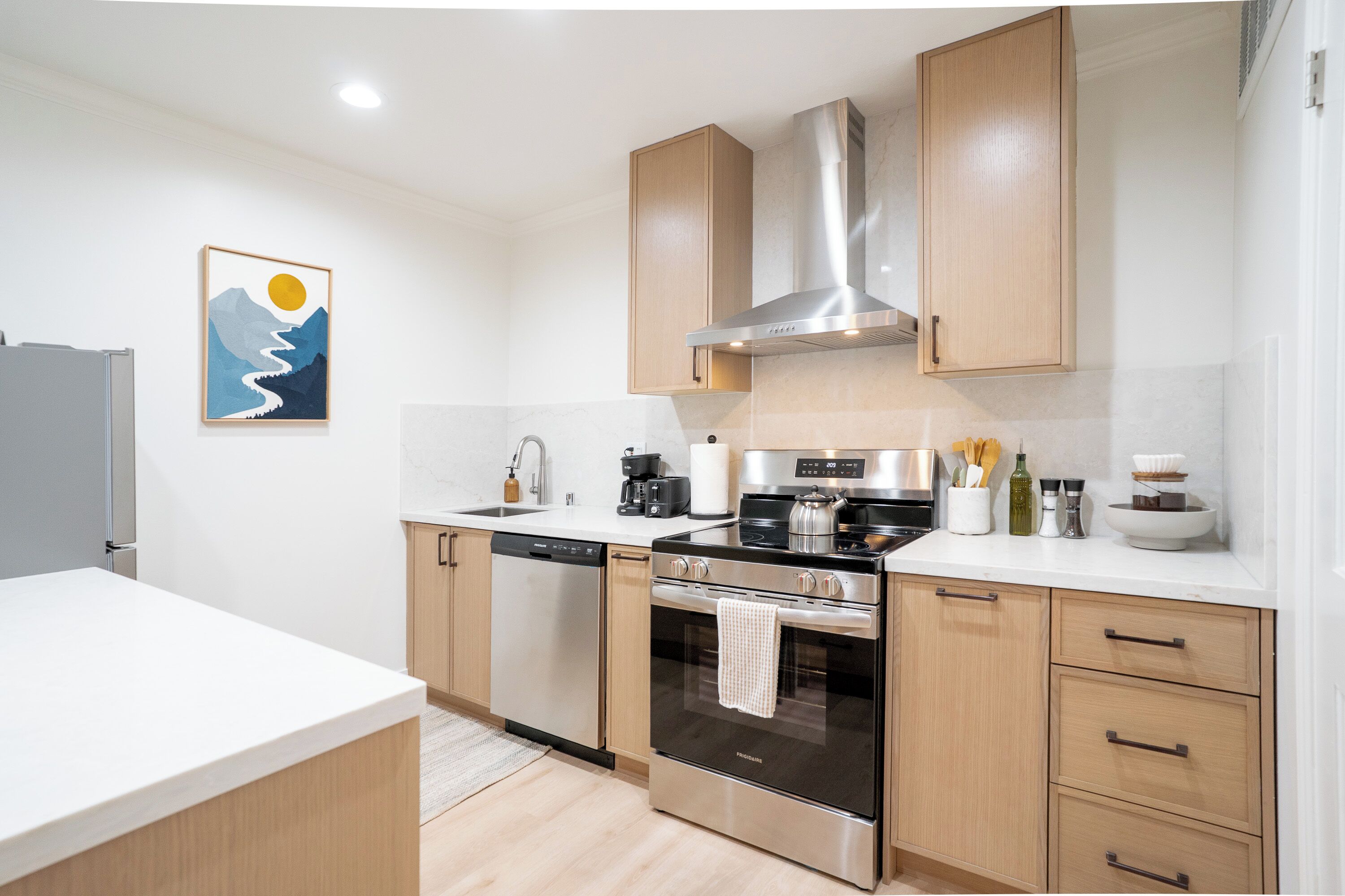 A modern kitchen with stainless steel appliances, wooden cabinets, and a white countertop.