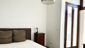 Un dormitorio con una cama, una mesita de noche, una lámpara y una puerta que da a un espacio al aire libre.