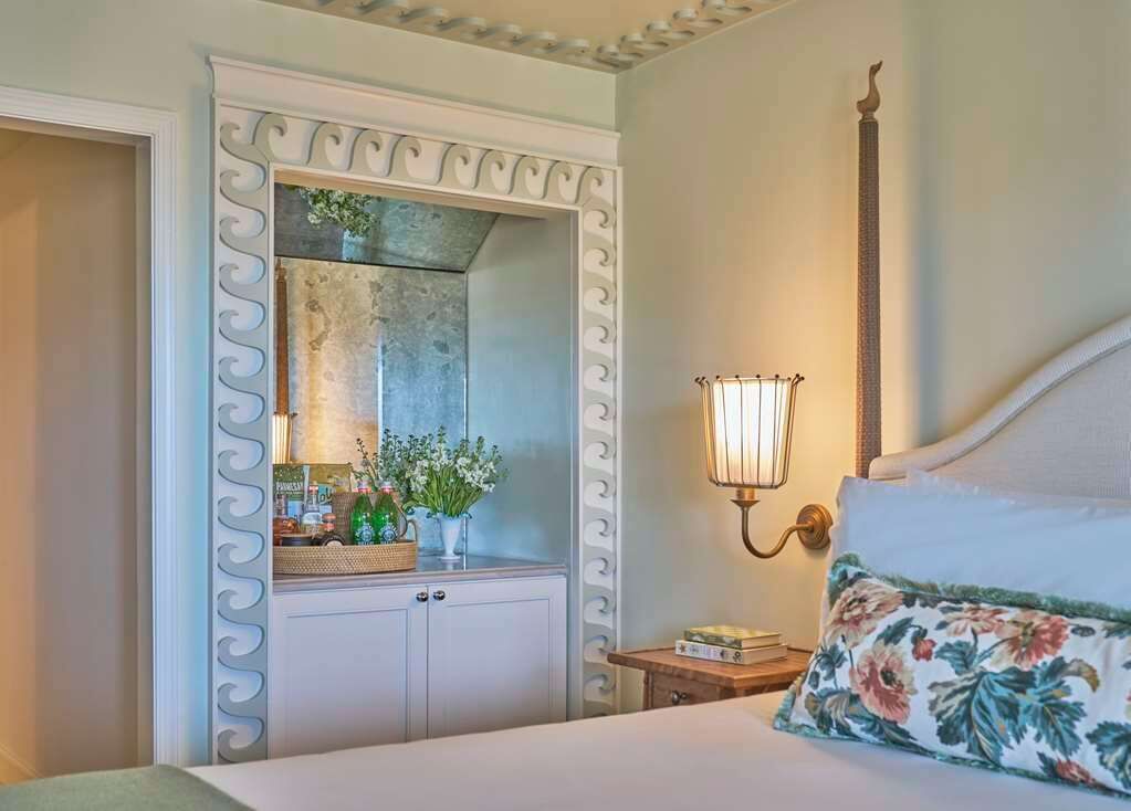 A bedroom with a bed, a nightstand, a mirror, and a wall-mounted lamp.