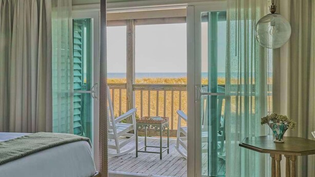 Une chambre avec une grande fenêtre donnant sur un balcon d’où l’on peut admirer la plage.
