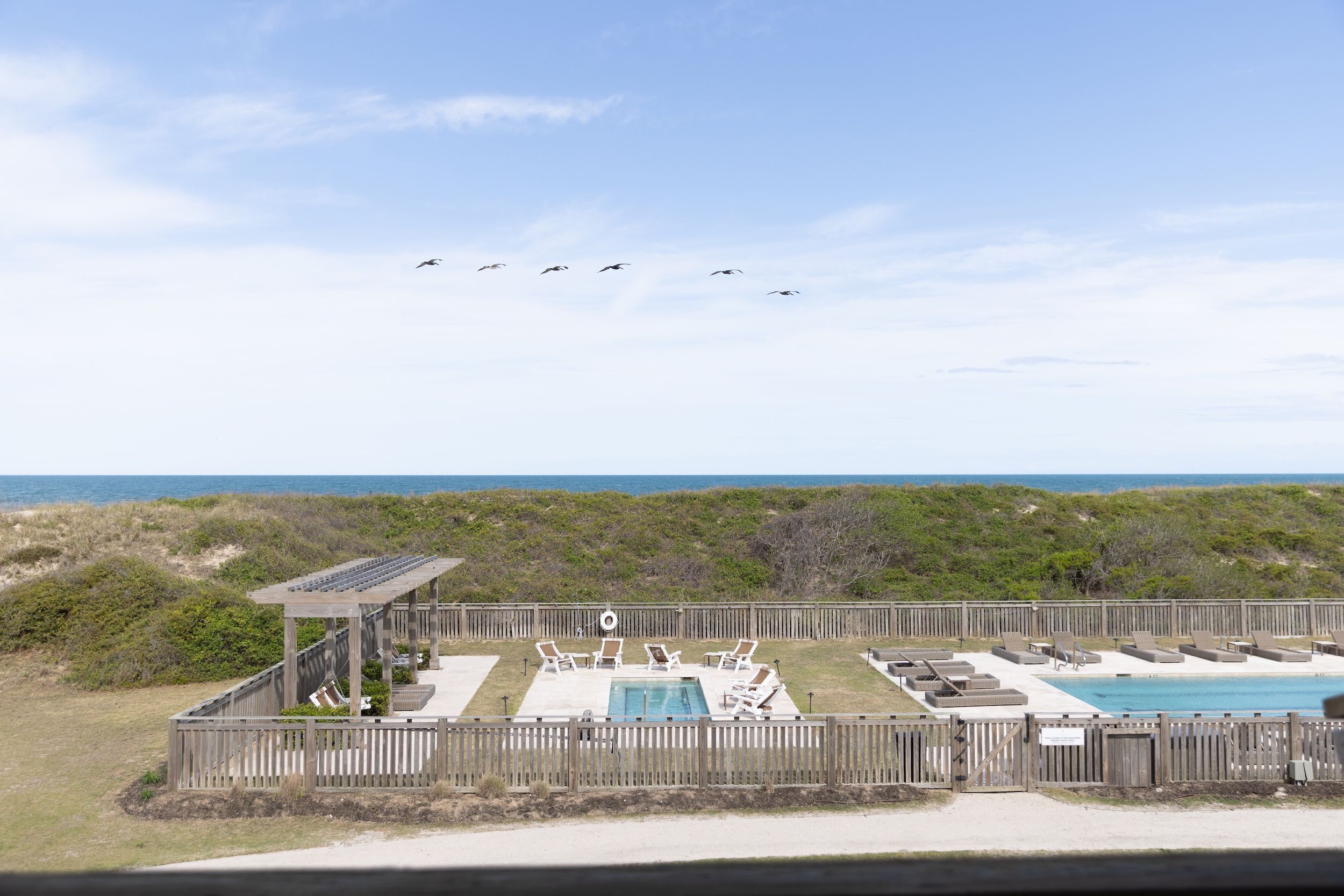 Zona de piscina con sillones de descanso, una pérgola y vista al océano.