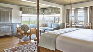 A spacious bedroom with a large bed, a sitting area with a sofa and chairs, and a view of the ocean through large windows. - Premium King | Oceanview + Award-Winning Spa (Duck)