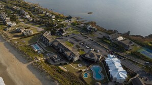 An aerial view of a coastal resort with a swimming pool, beach access, and a marina. - Premium King | Oceanview + Award-Winning Spa (Duck)