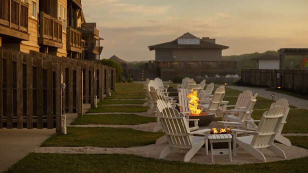 A row of Adirondack chairs with a fire pit in the center, set on a gravel path with a wooden fence on one side. - Oceanside King Suite | Near Pool + Private Beach (Duck)