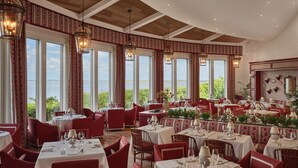 A restaurant with multiple tables, red chairs, and large windows offering a view of the sea. - Oceanside King Suite | Near Pool + Private Beach (Duck)