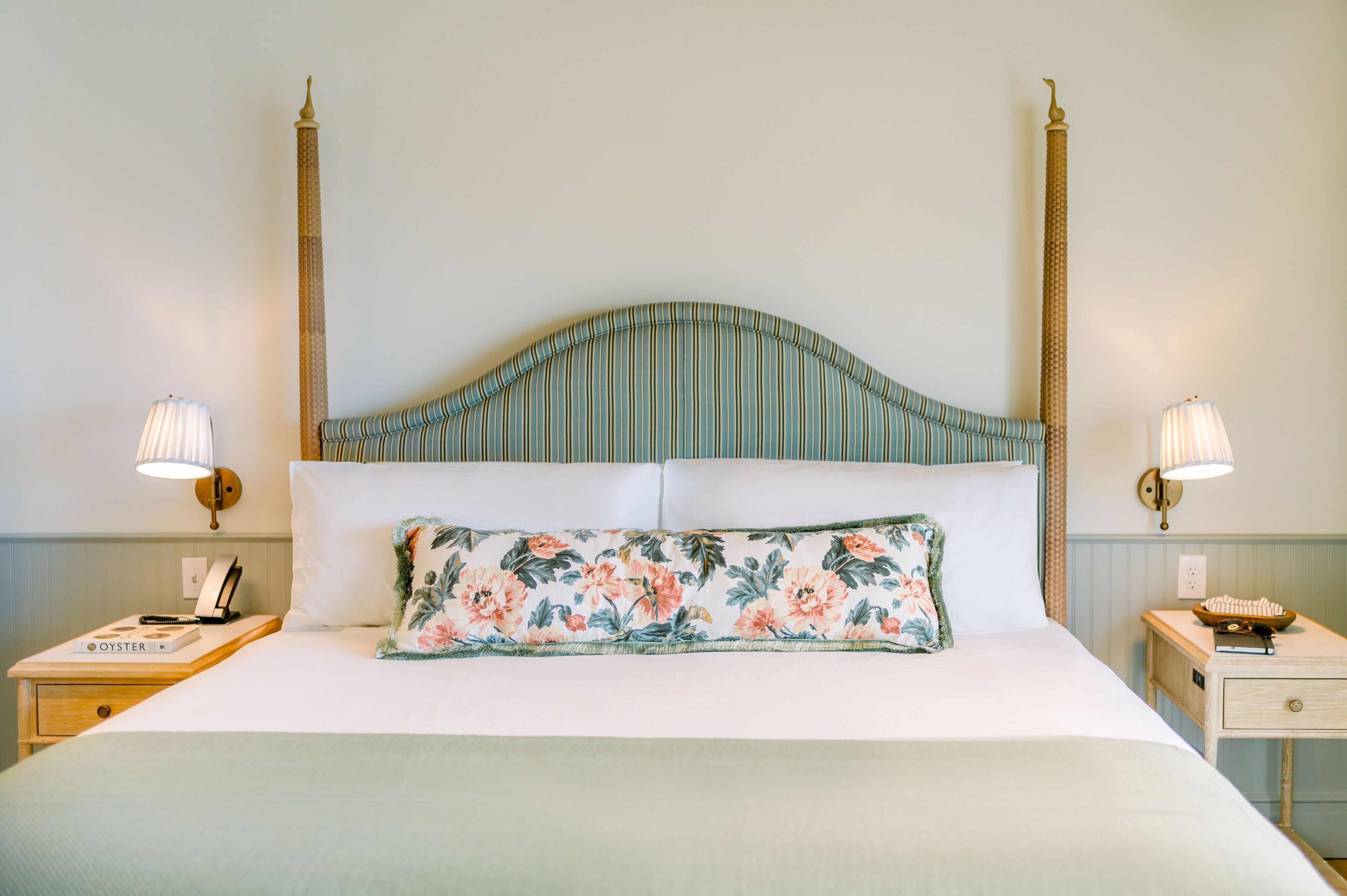 A bed with a floral pillow, two bedside tables with lamps, and a tall, striped headboard.