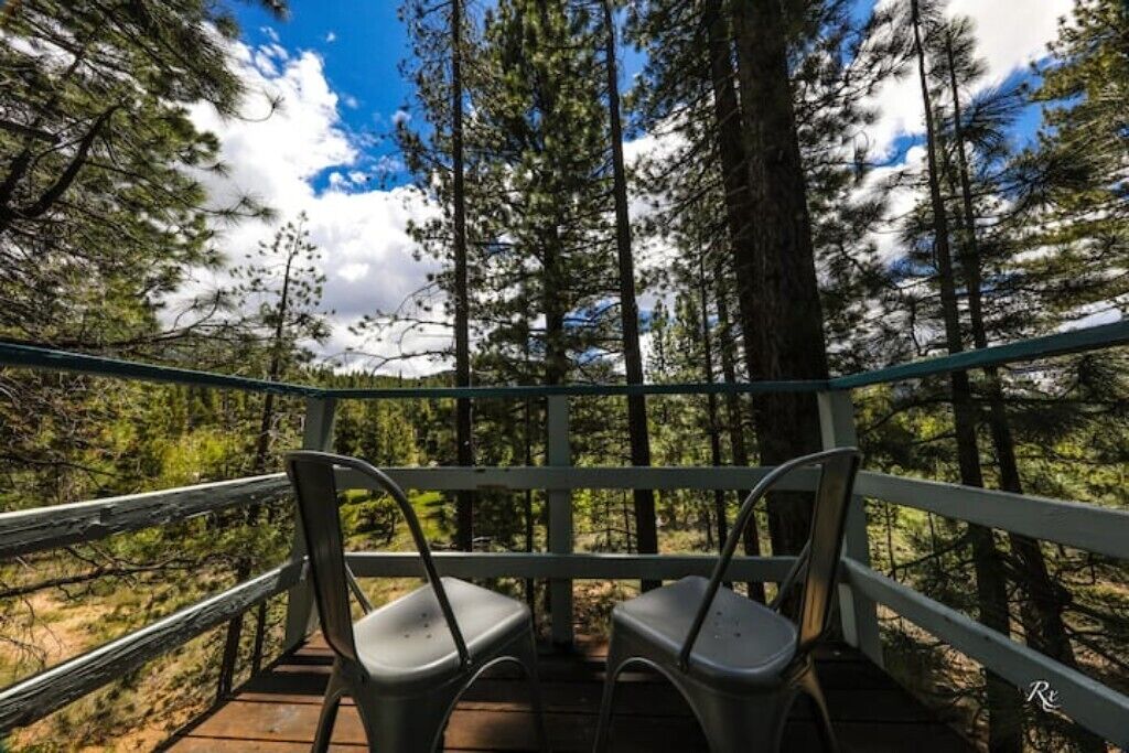 Une terrasse en bois avec des chaises en métal, donnant sur une forêt.
