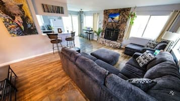 Una sala de estar moderna con un sofá seccional, una chimenea y un comedor con taburetes de bar.
