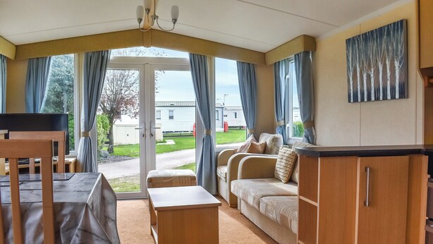 Ein gemütliches Zimmer mit einer Couch, einem kleinen Tisch und einem Fernseher. Ein Fenster mit Vorhängen und ein Bild an der Wand sind ebenfalls vorhanden.