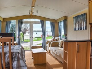 Une pièce confortable avec un canapé, une petite table et un téléviseur. Il y a une fenêtre avec des rideaux et un tableau au mur.