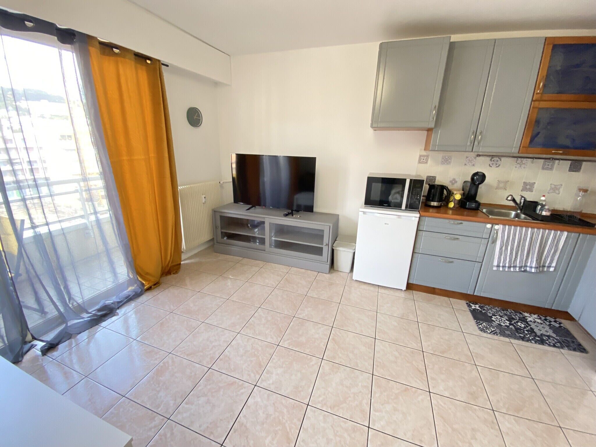 A compact living space with a kitchenette, a flat-screen TV, and a small refrigerator.