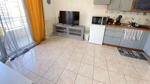 Un espace de vie compact comprenant une kitchenette, un téléviseur à écran plat et un petit réfrigérateur.