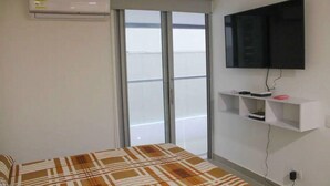Une chambre à coucher avec un lit, un téléviseur fixé au mur, une fenêtre et un climatiseur mural.
