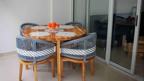Une table ronde en bois, quatre chaises en osier, une porte en verre et un sol carrelé.