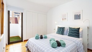 Quarto com cama, porta para uma varanda e um pequeno hall de entrada.