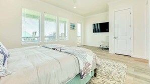 A bedroom with a bed, a TV, a door, and large windows. - New 5BR Beach House with Dual Decks and Fire Pit (Surfside Beach)